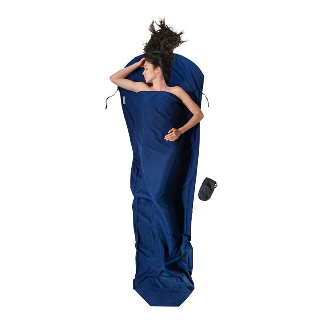 Mujer acostada en un saco de dormir azul, en posición lateral, con una bolsa de tela al lado.